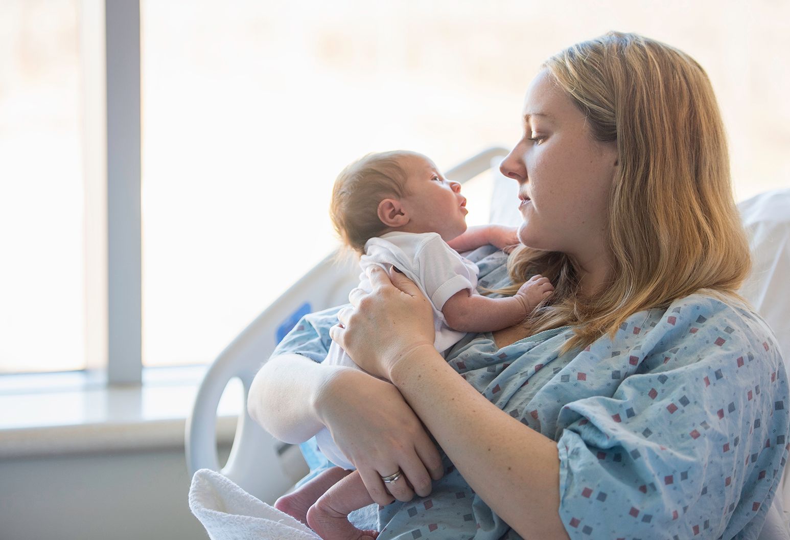 Mother in a hospital bed holding her beautiful newborn baby looking into the baby's eyes.